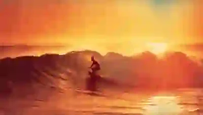 Silhouette of a surfer riding a wave at sunset with an orange and yellow sky.